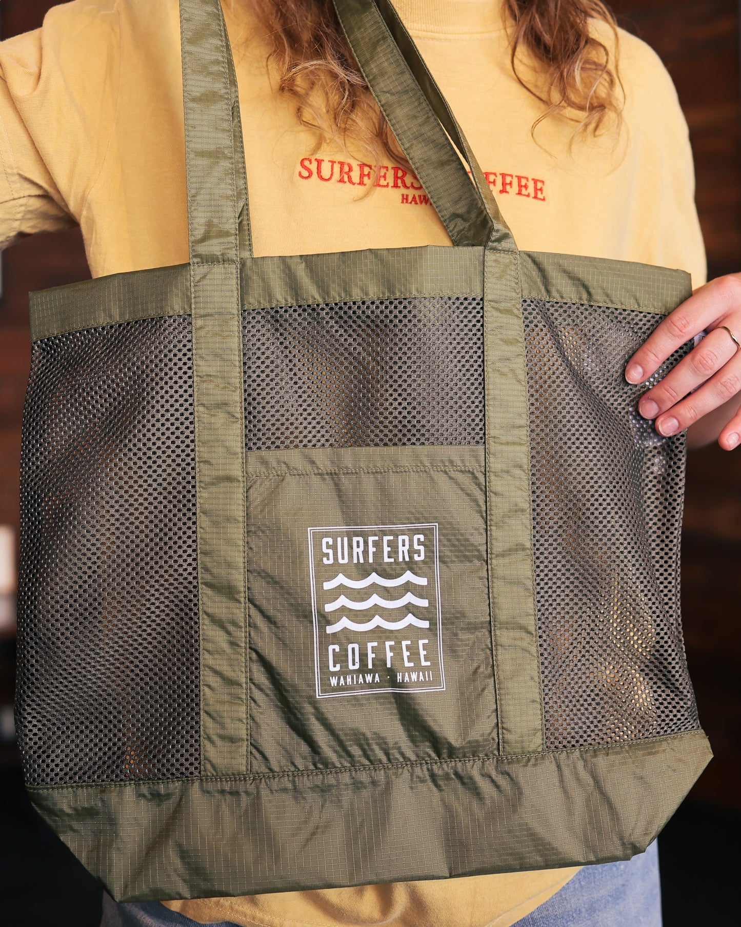 Green tote bag with 'Surfers Coffee' logo held by a person wearing a yellow shirt.