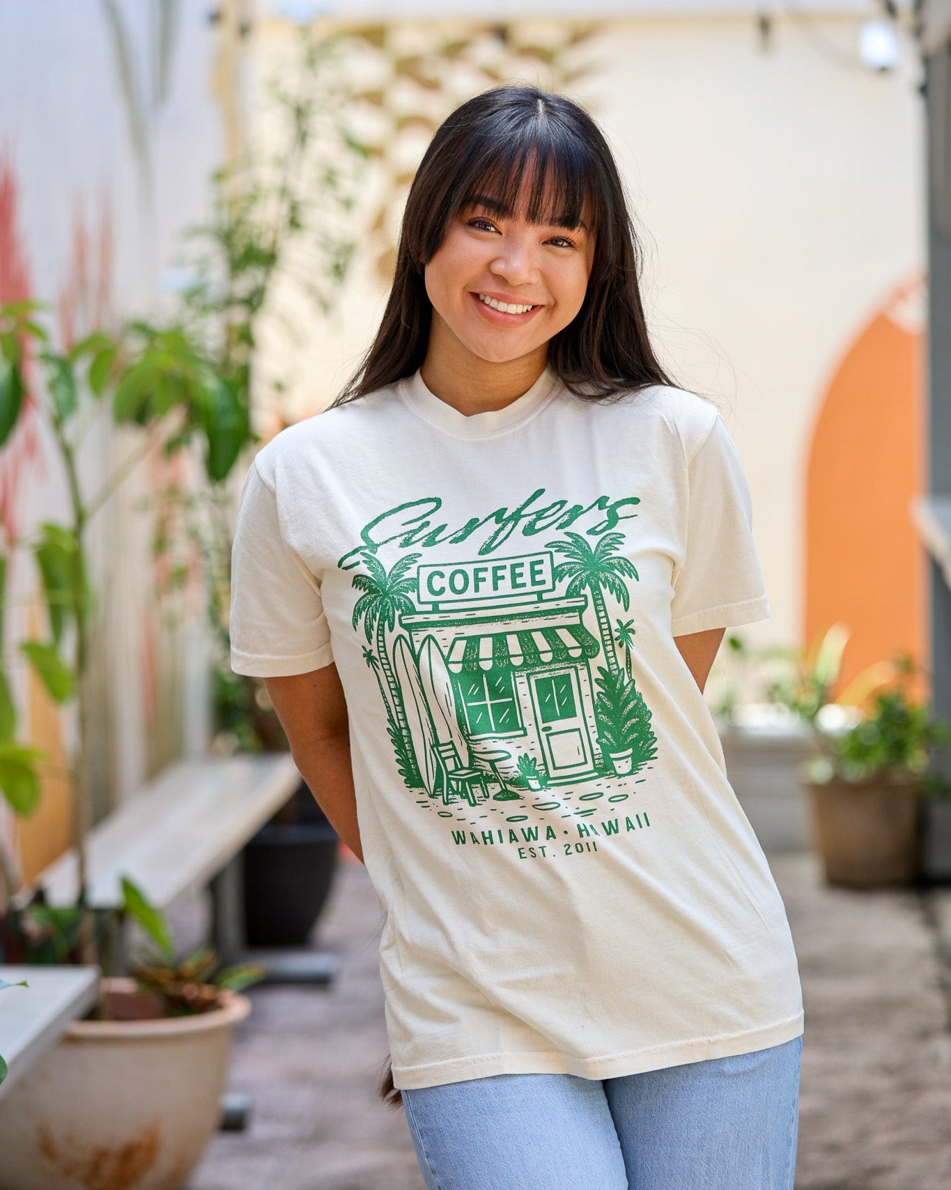 Woman wearing a t-shirt with a graphic design of a coffee shop and text, standing outdoors.