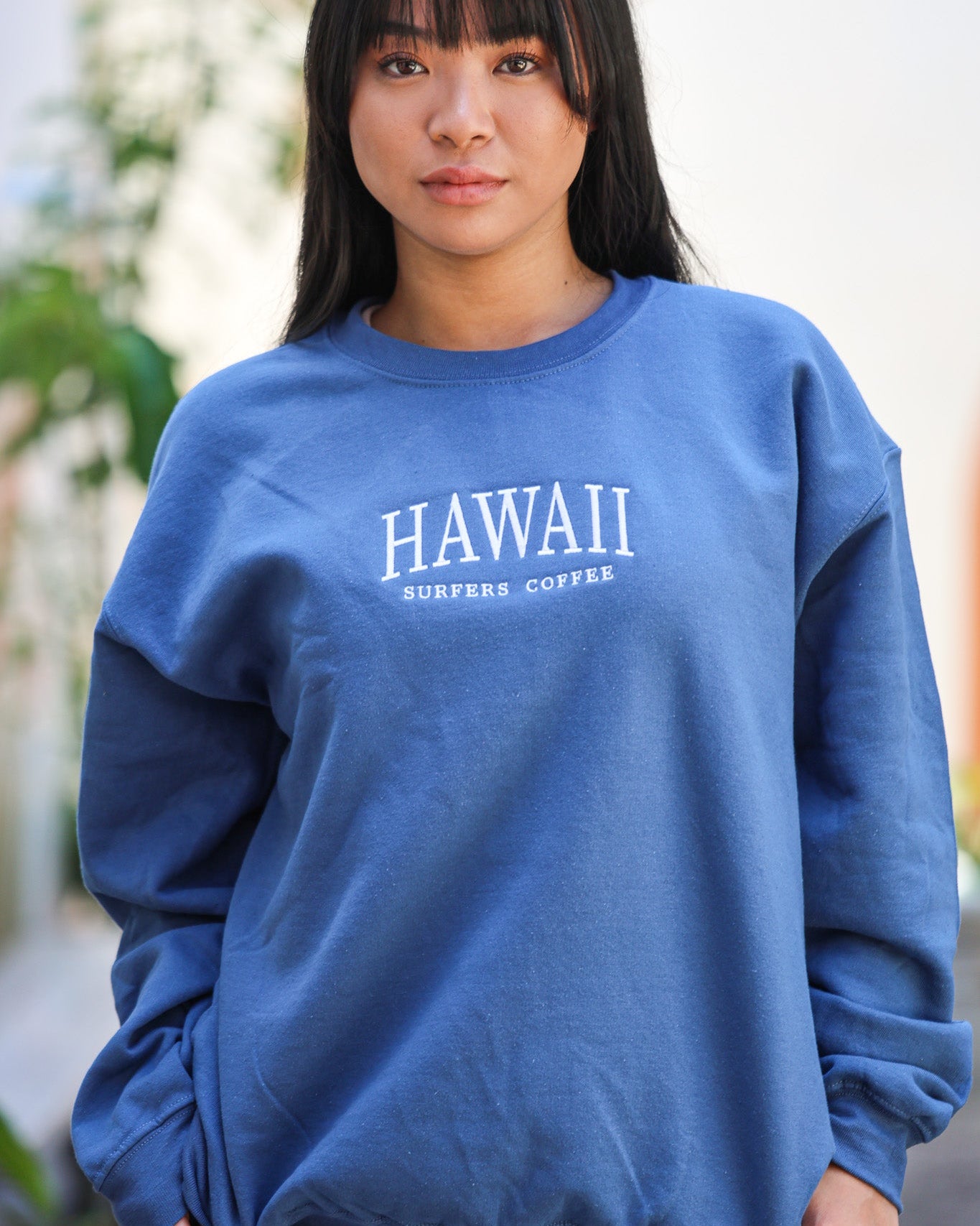 Person wearing a blue sweatshirt with 'HAWAII' printed on it, standing outdoors.