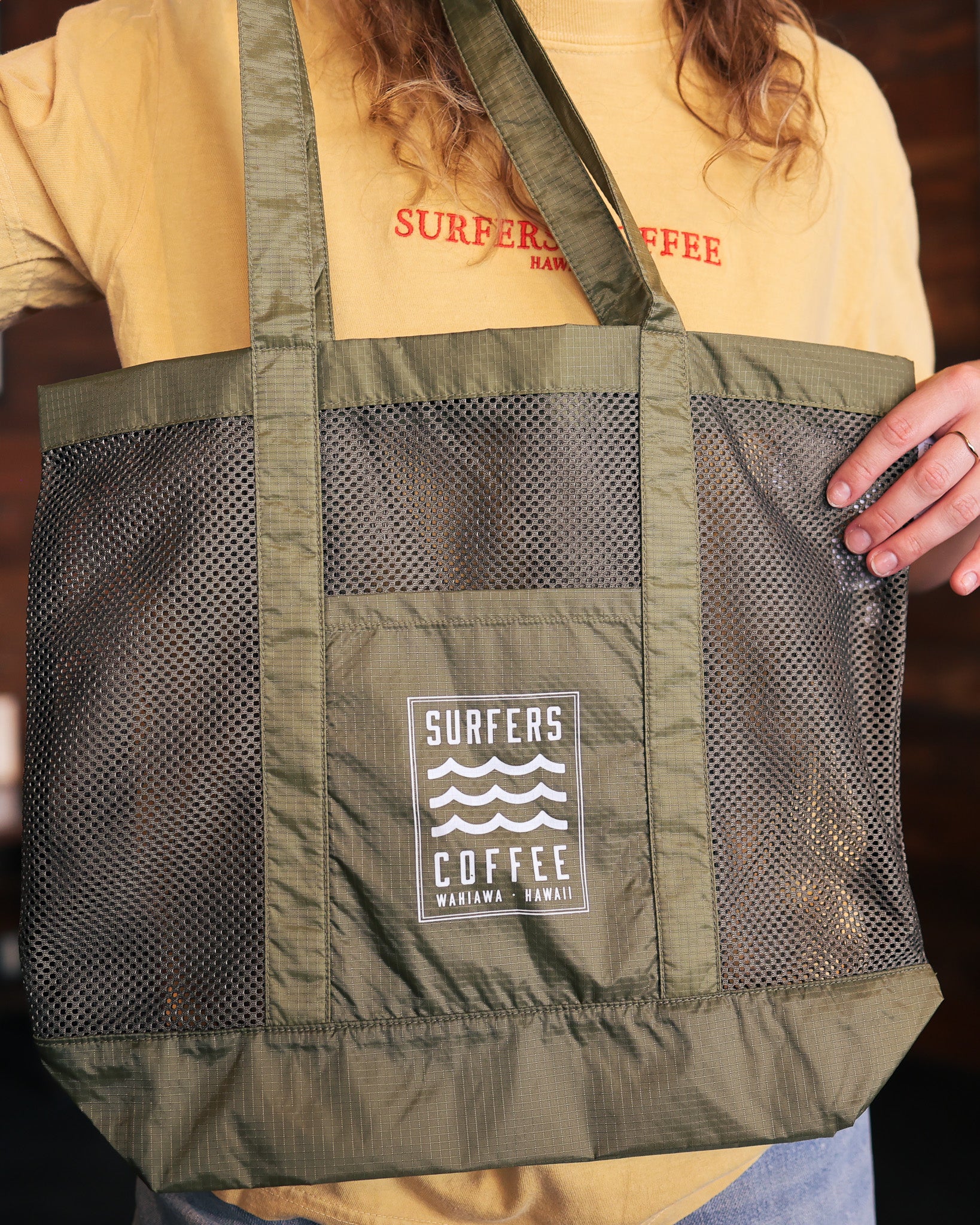 Green tote bag with 'Surfers Coffee' logo held by a person wearing a yellow shirt.