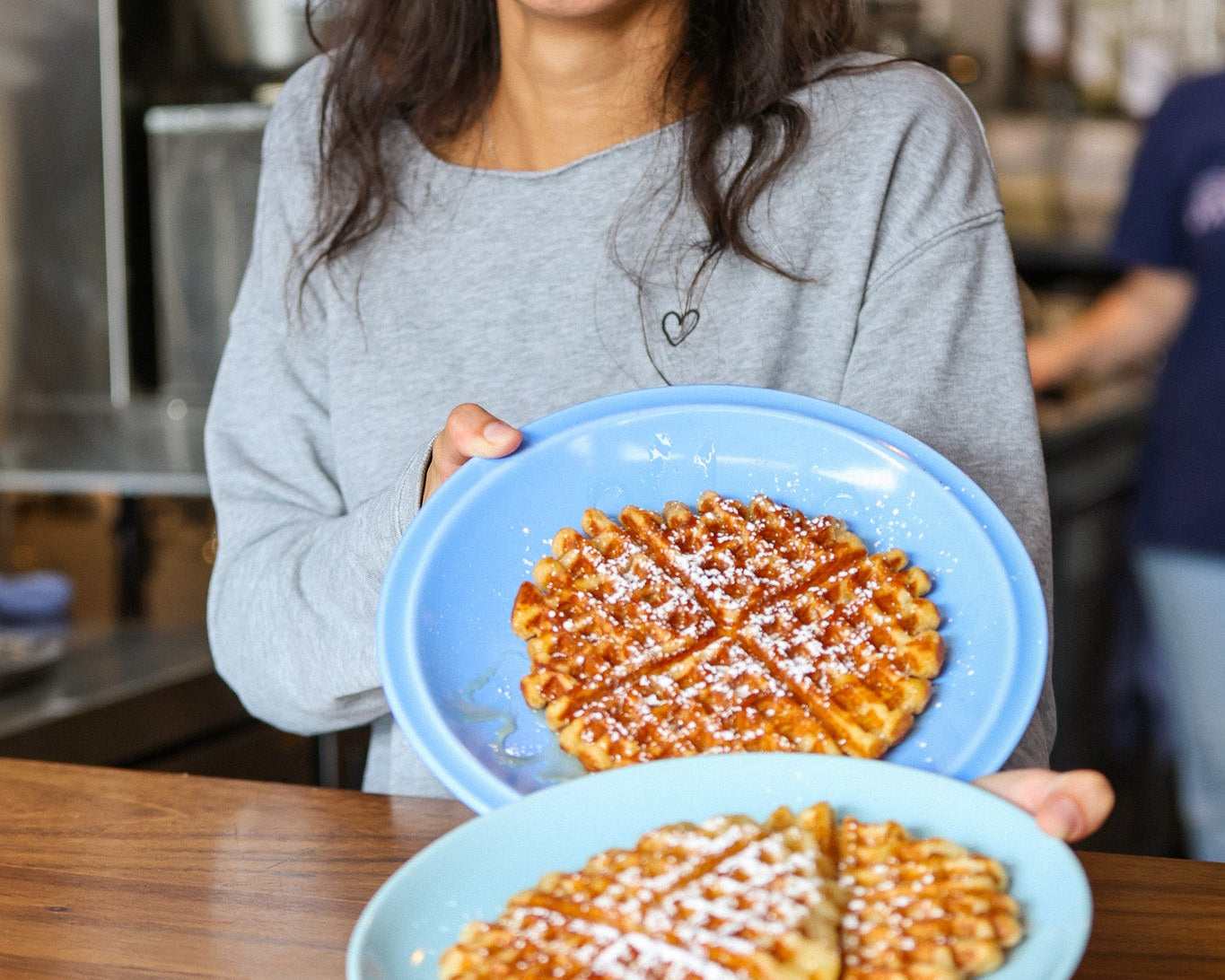 Person holding two plates of waffles in a kitchen setting
