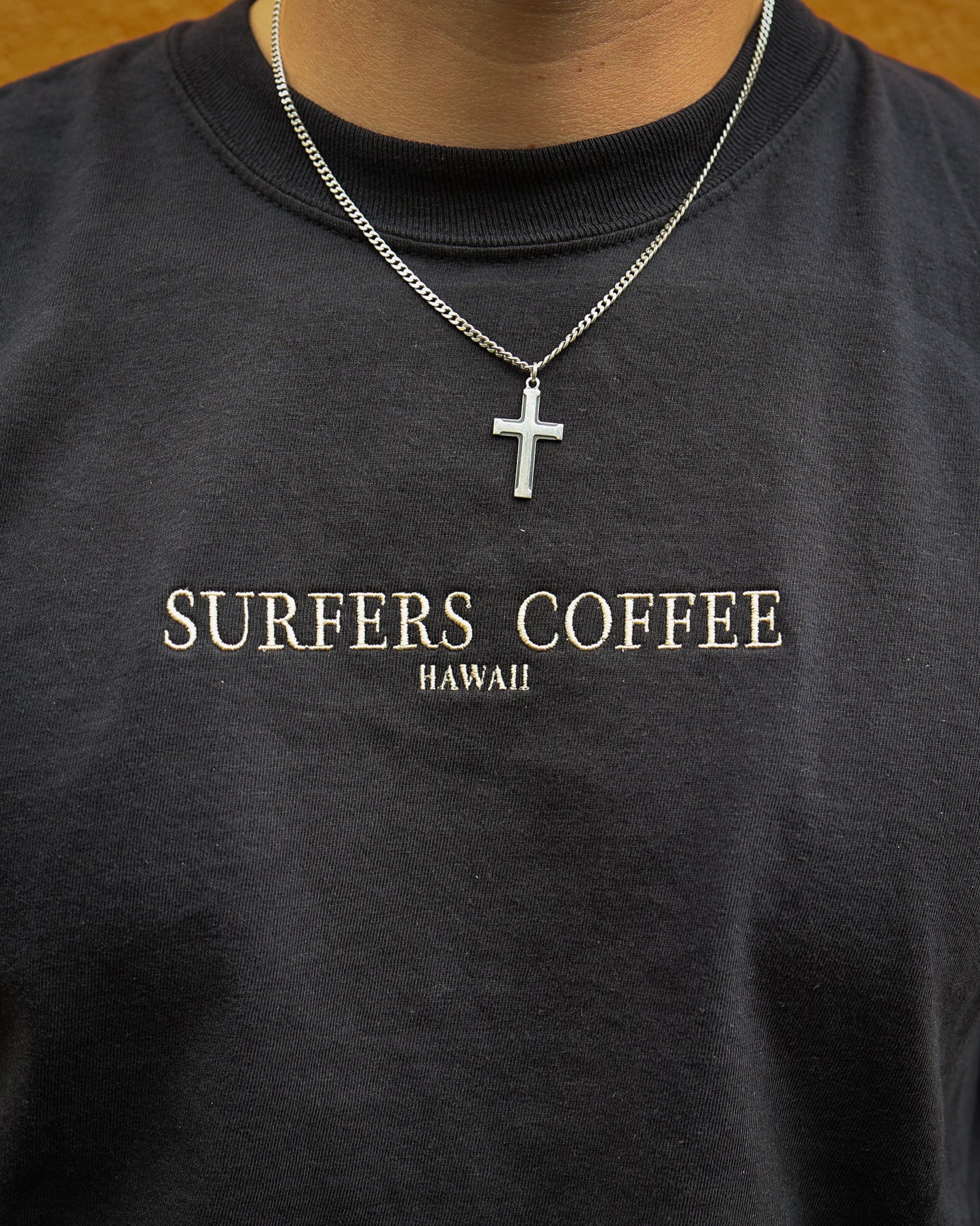 Black shirt with 'Surfers Coffee Hawaii' text and a necklace with a cross pendant.