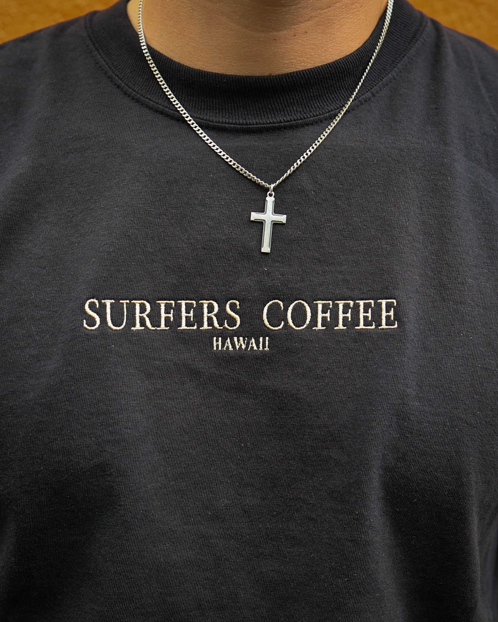 Black shirt with 'Surfers Coffee Hawaii' text and a necklace with a cross pendant.