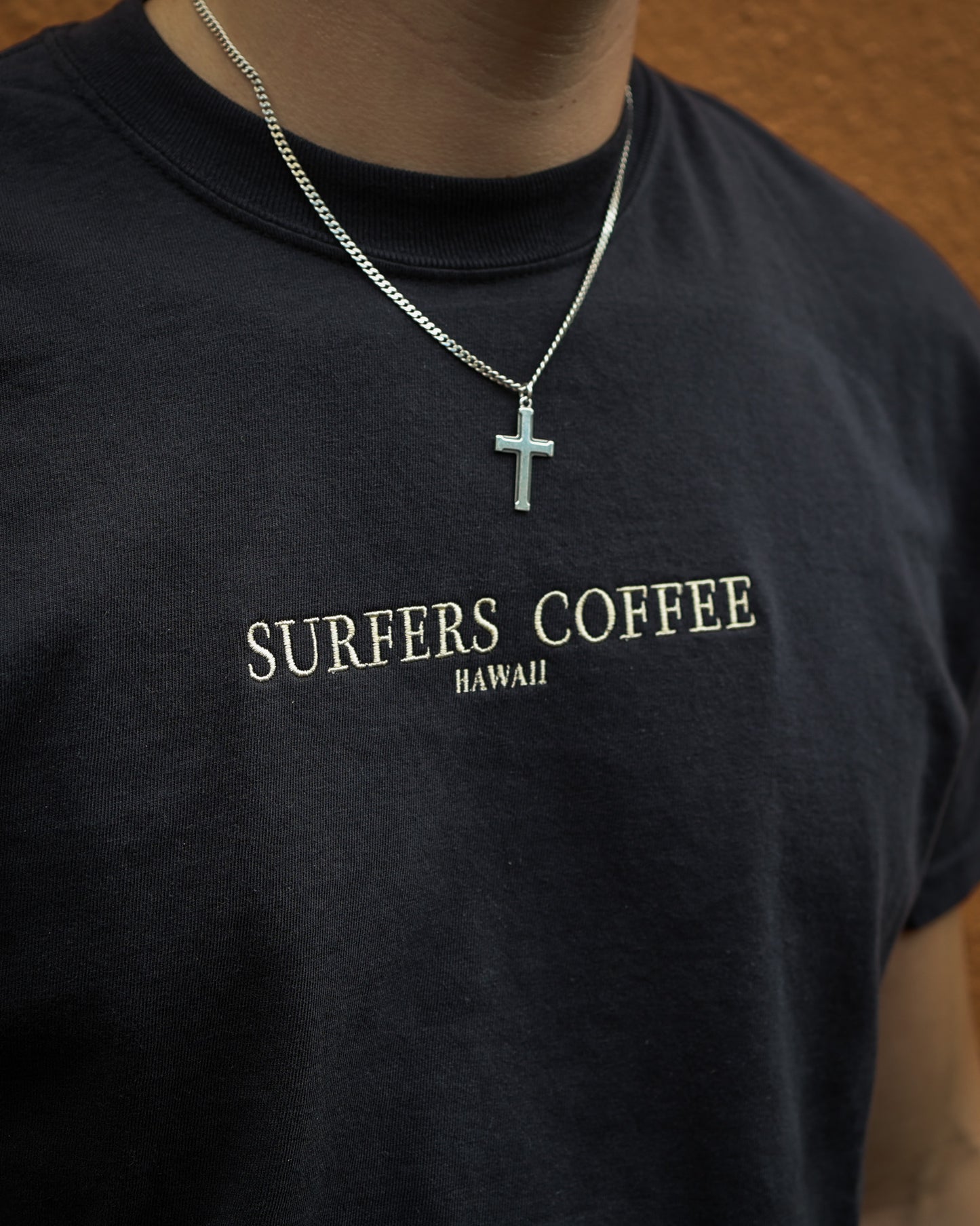 Black t-shirt with 'Surfers Coffee Hawaii' text and a necklace with a cross pendant.