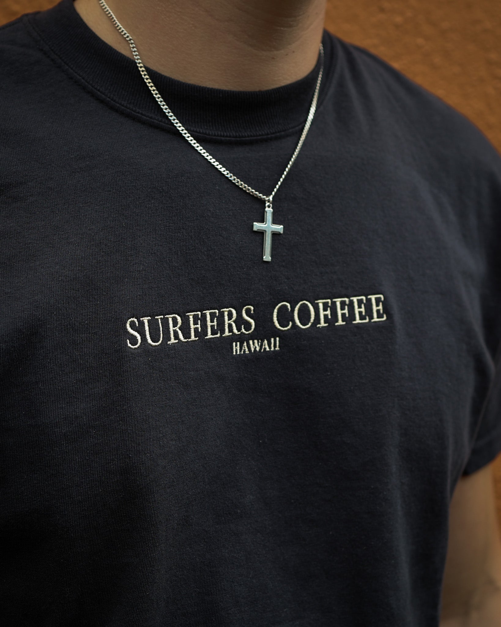 Black t-shirt with 'Surfers Coffee Hawaii' text and a necklace with a cross pendant.