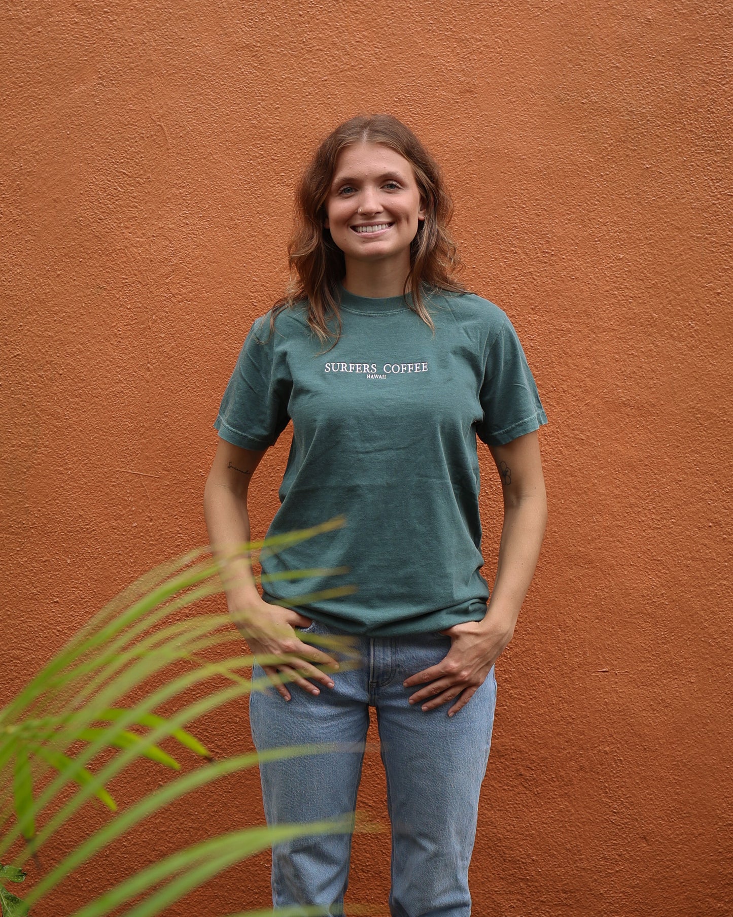 Woman wearing a green t-shirt with text, standing against an orange wall.