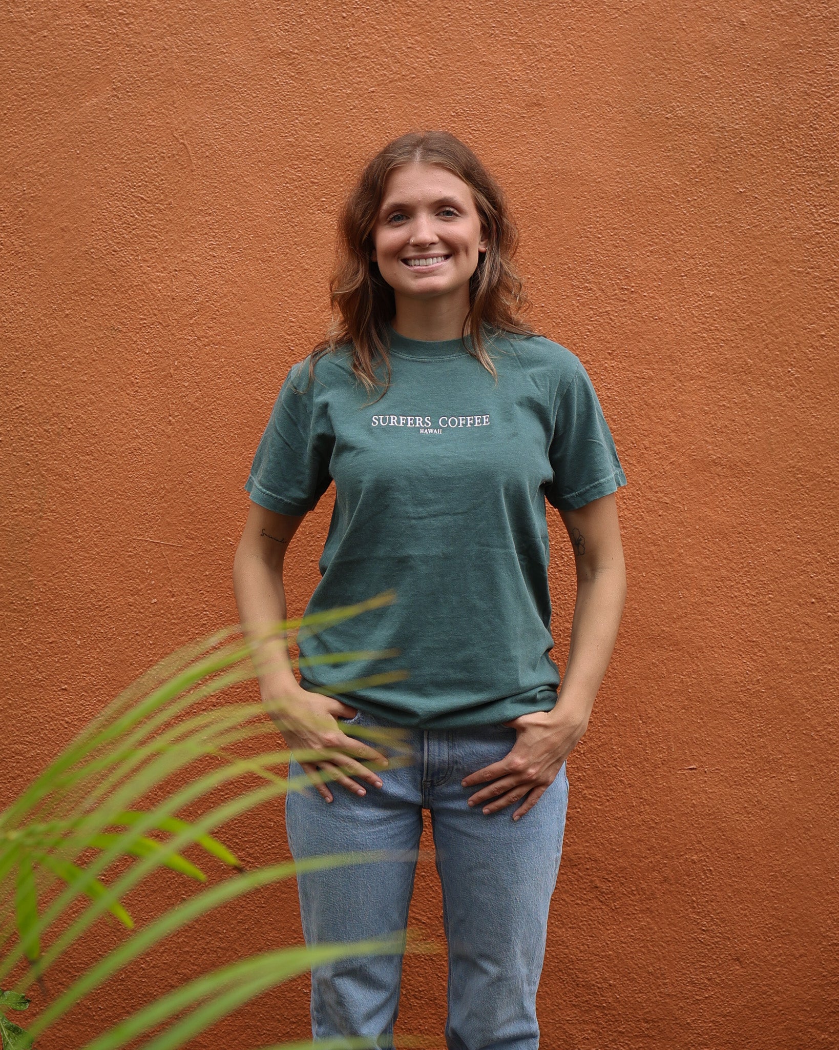 Woman wearing a green t-shirt with text, standing against an orange wall.