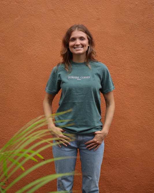 Woman wearing a green t-shirt with text, standing against an orange wall.