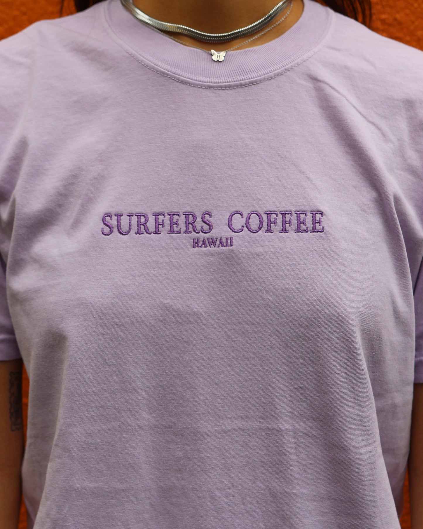 Purple t-shirt with 'Surfers Coffee Hawaii' text on a plain background