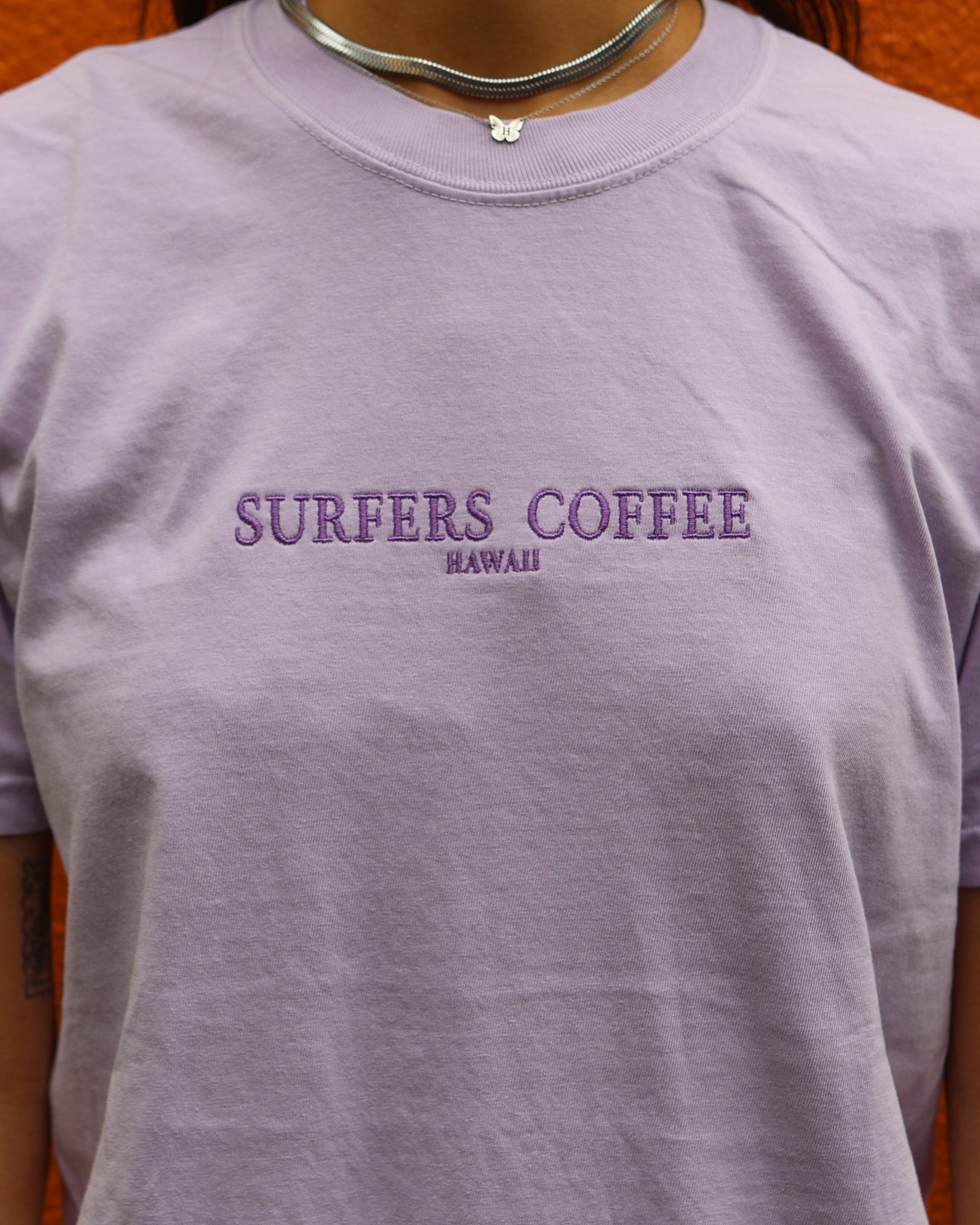 Purple t-shirt with 'Surfers Coffee Hawaii' text on a plain background